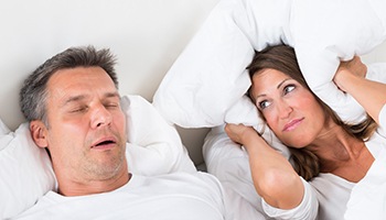 Frustrated woman in bed next to snoring man