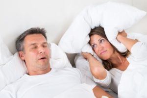 woman covering ears while man snore