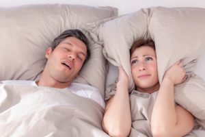 a man snoring and a woman with a pillow covering her ears